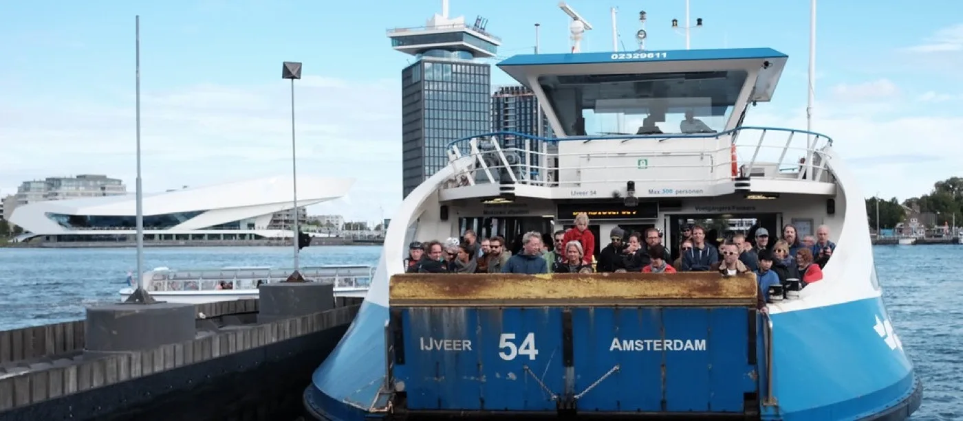 Crowded GVB ferry IJveer 54 docking on the IJ with the EYE Film Museum and A'DAM Tower in the background