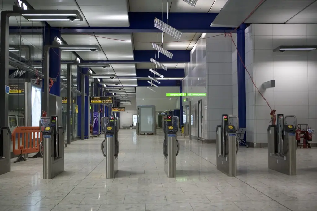 Empty rows of contactless ticket gates stretching down a tiled transit-station corridor under blue ceiling beams