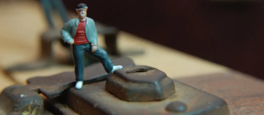Miniature figurine of a traveller in red shirt standing on a rusted railway track bolt, shot in macro