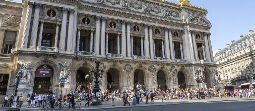 Crowds gathered on the steps of the Palais Garnier opera house in Paris under bright sunlight